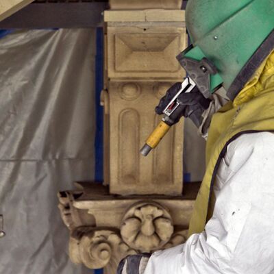 Ein Arbeiter in Schutzkleidung restauriert die Natursteinfassade mit dem Partikel-Strahlverfahren.